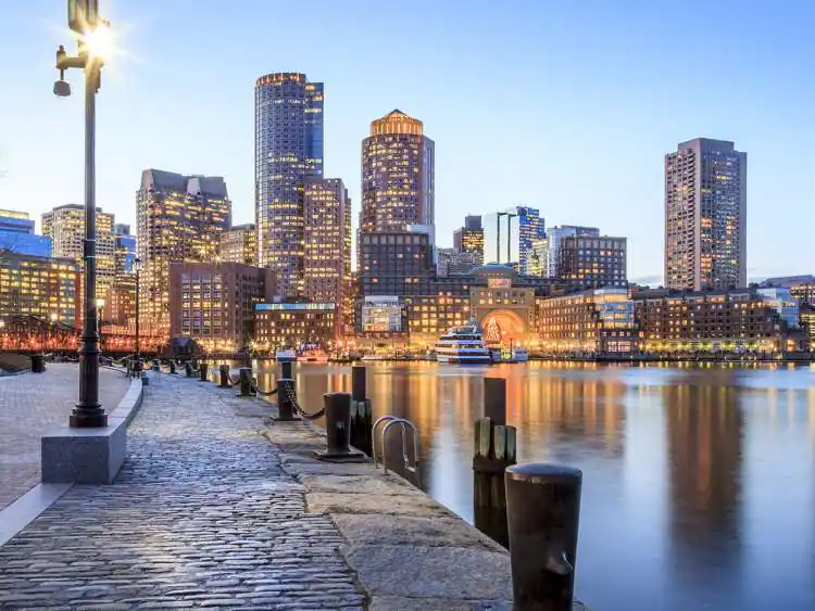 the edge of the water with a cobblestone path and big buildings in the back of the city of Boston Massachusetts