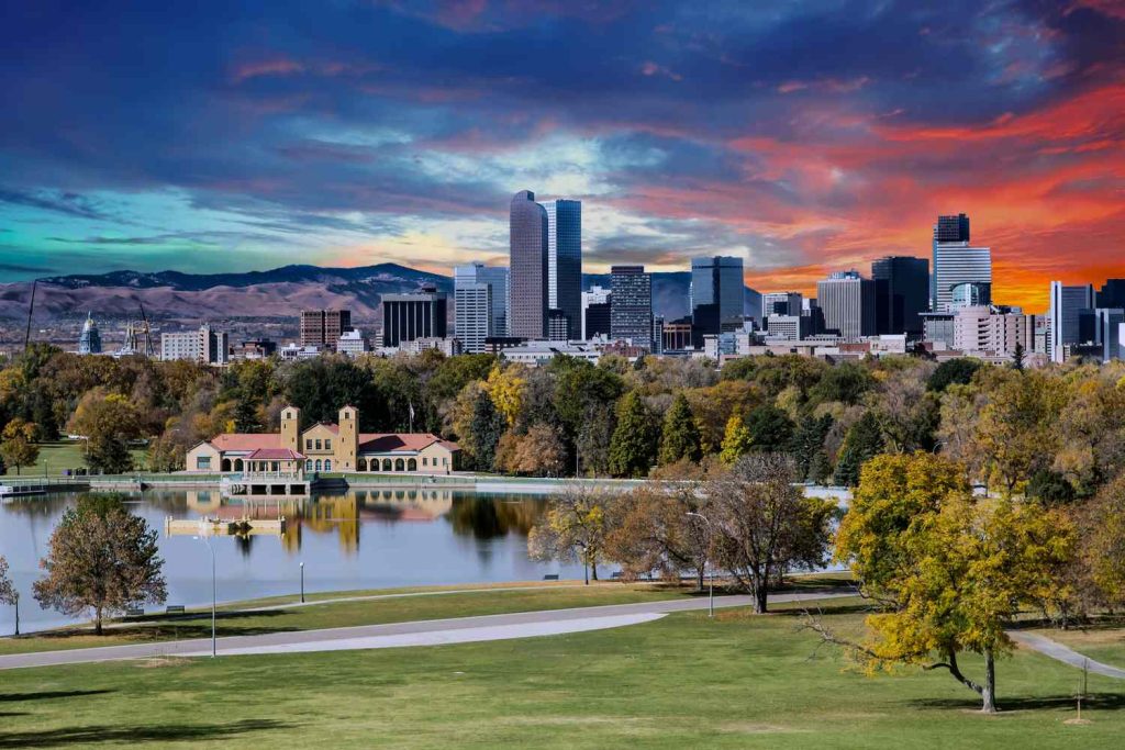 The mountains and sunset in Denver Colorado with big buildings and a pond in the front
